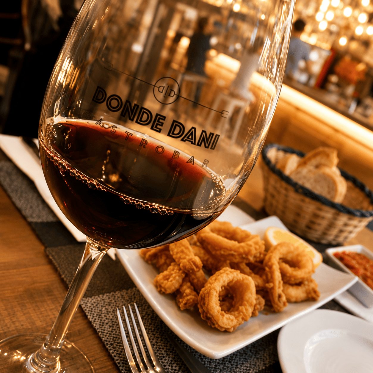 Copa de vino tinto serigrafiada con el logo de Donde Dani junto a una ración de calamares