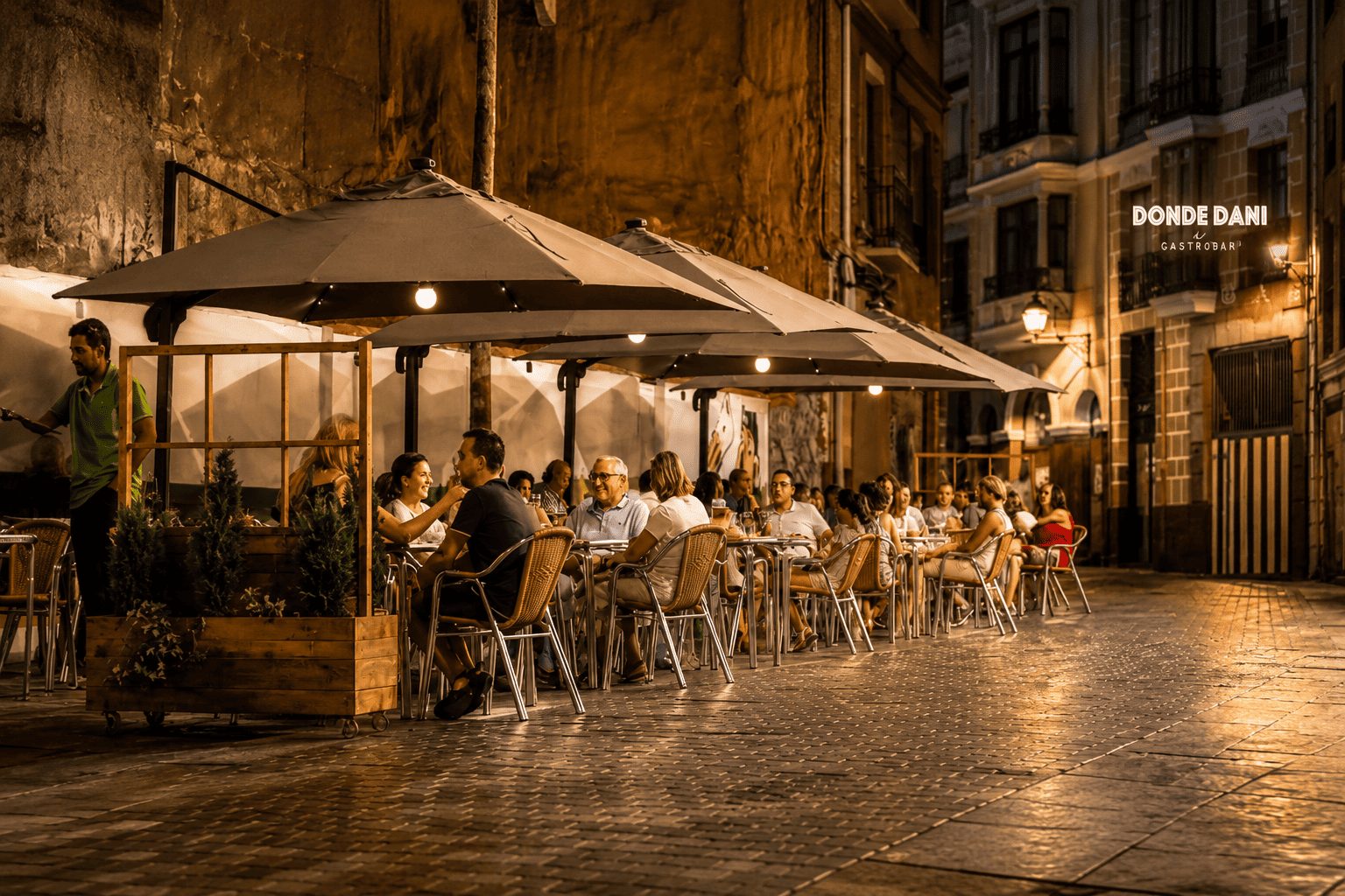 Terraza de Donde Dani de noche, con mesas llenas bajo las sombrillas en la calle empedrada